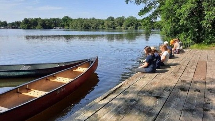 Menschen sitzen am Steg in der Nähe von Kanus.