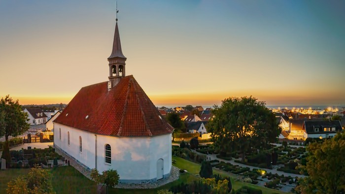 En hvid kirke med rød tag og tårn i en landsby ved sundet
