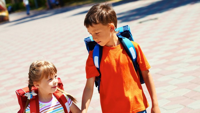 Junge mit Schulrucksack, an seiner Hand ein kleines Mädchen mit Schulrucksack