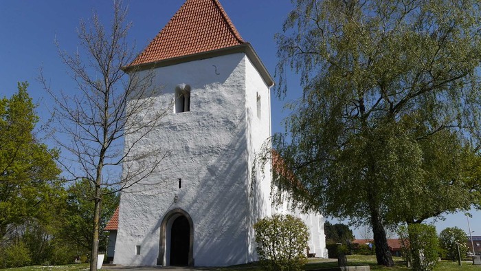 Eine weiß gekalkte Kirche mit gedrungenem Turm vor blauem Himmel