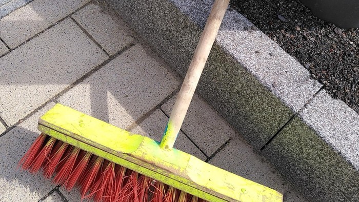 Ein Besen mit roten Borsten auf Steinplatten gelegt.