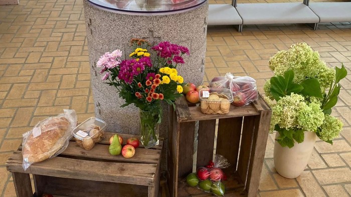 Billede af blomster, brød og frugter på trækister og bænke.
