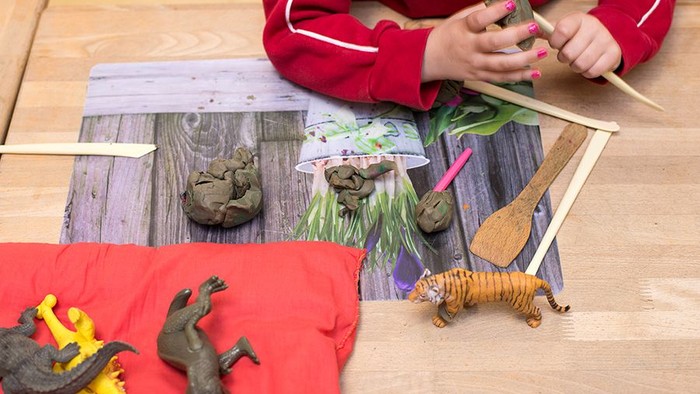 Ein Kind spielt mit Spielzeugtieren und natürlichen Gegenständen auf einem Holztisch.