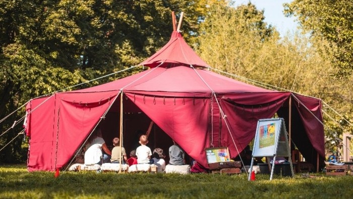 Eine lebhafte rote Zeltplane auf einer grünen Wiese im Park, um die sich Menschen versammelt haben und eine Outdoor-Veranstaltung oder ein Treffen genießen.