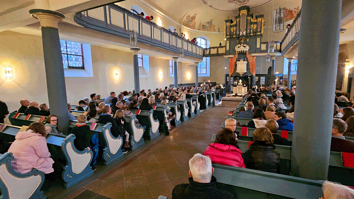 Überfülltes Kircheninneres mit Teilnehmern, die während eines Gottesdienstes oder einer Versammlung in den Bänken sitzen.