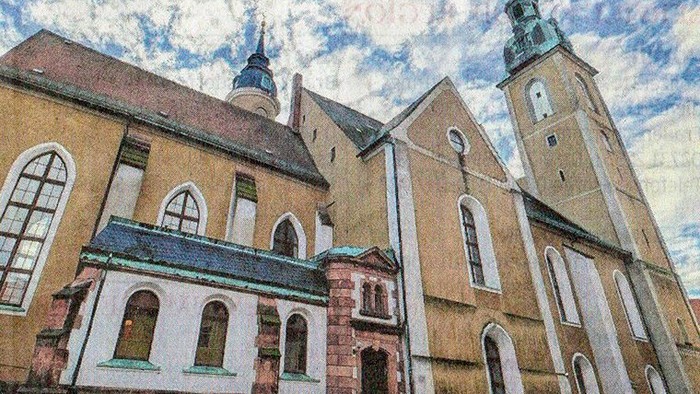 Historische Kirche mit gotischer Architektur, Zwillingstürmen und Bogenfenstern unter einem teilweise bewölkten Himmel.