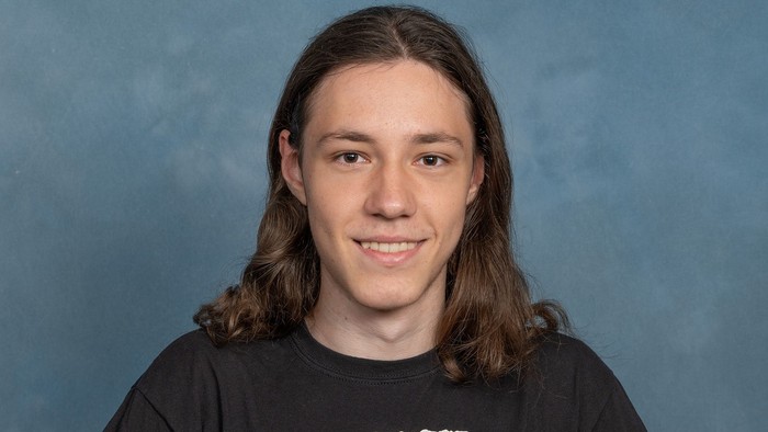 Porträt eines lächelnden jungen Mannes in einem schwarzen T-Shirt mit weißem Text und Grafiken.