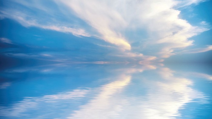 En serene og klart himmelblå hav med flaue skyer og deres refleksioner i vandet