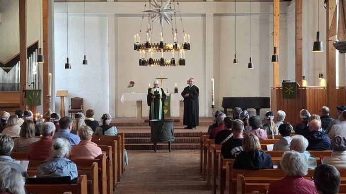 Ein Gottesdienst mit Geistlichen, die vor Gläubigen stehen, die auf hölzernen Kirchenbänken aufmerksam zuhören.