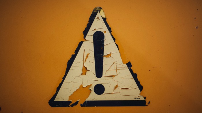 Dreieckiges Warnschild mit Ausrufezeichen auf einer orangefarbenen Wand.