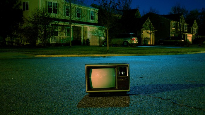 Ein alter Röhrenfernseher liegt auf einer Autostraße in einer Wohngegend bei Nacht.