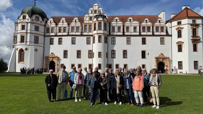 Eine Gruppe von Menschen, die vor einem prächtigen historischen Schloss an einem strahlend sonnigen Tag posieren.