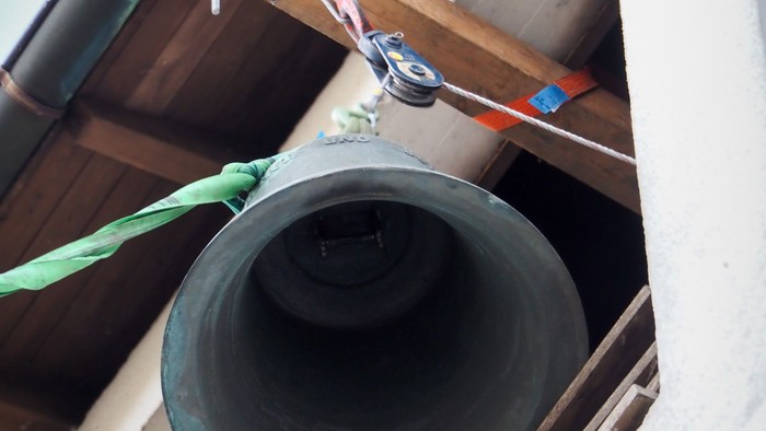 Eine Glocke wird an einem Seilzug aus einem Turmfenster gehoben