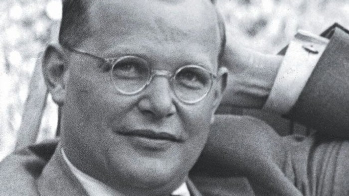 Ein Mann mit Brille und Anzug posiert im Freien und wirkt nachdenklich und gelassen in einem vintage Schwarz-Weiß-Foto.