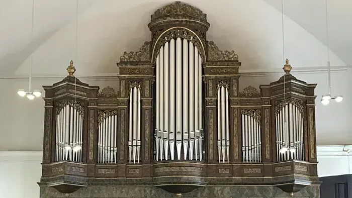 Elegante historische Pfeifenorgel mit aufwendiger Holzschnitzerei und verzierten Details in einer prächtigen Kirchenkulisse.