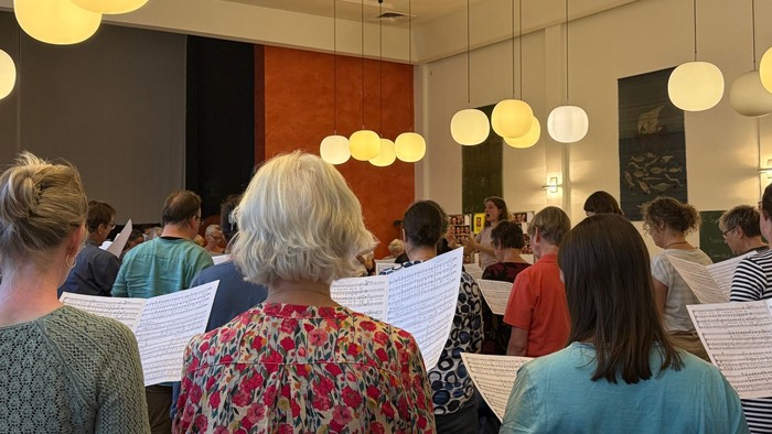 Ein probender Chor, von hinten fotografiert - mit Hinterköpfen und Liedzetteln.