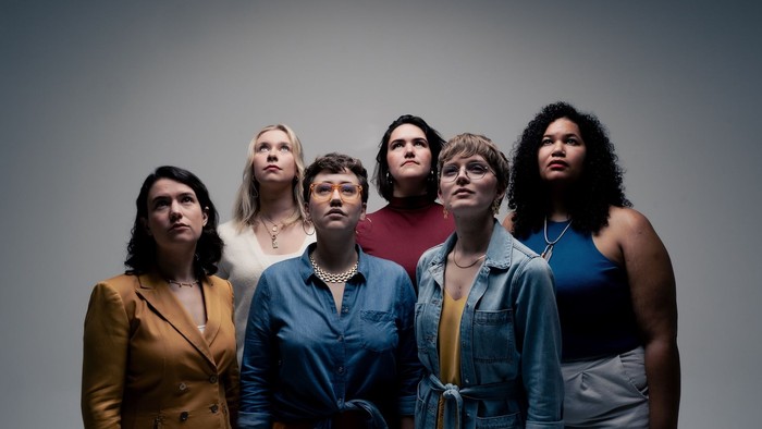 Eine gemischte Gruppe Frauen schaut nach oben, vor grauem Hintergrund