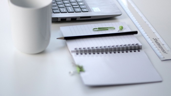 Bureau med laptop, kaffe, blok, pen og linieal