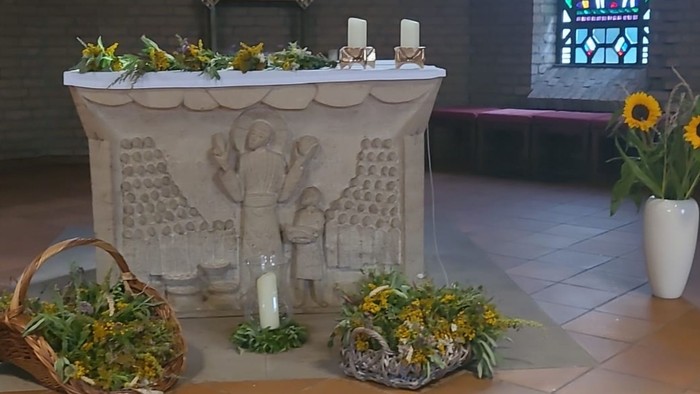 Geschmückter Altar mit Blumengestecken, Kerzen und religiösen Schnitzereien in einer besinnlichen Kirchenatmosphäre.