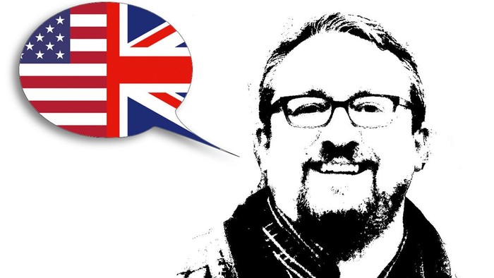 Mann mit Brille und Bärtchen, daneben Sprechblase mit US- und UK-Flaggen