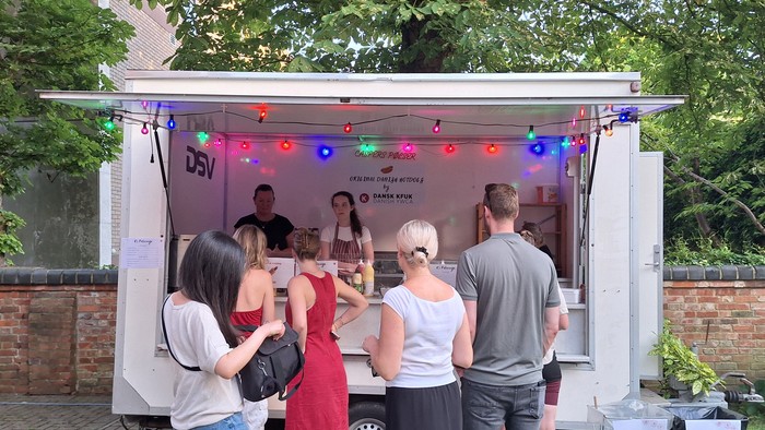 Folk samles omkring en mobil DJ-bod med farverige lys til en udendørs begivenhed.
