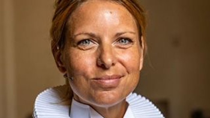 Kvinde i formelt tøj med en hvid krøllet krave og et professionelt, neutralt udtryk.