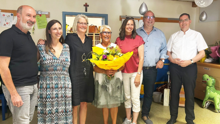 Eine Gruppe von Menschen, die gemeinsam posieren, wobei eine Person einen großen gelben Blumenstrauß in Innenräumen hält.