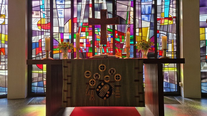 Altar mit Kreuz und vier großen Altarkerzen vor dem bunten Bleiglasfenster der Stephanus-Kirche