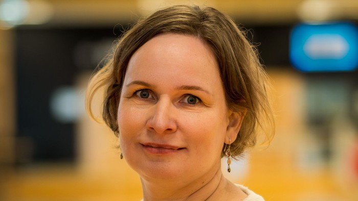 En smilende kvinde i en lys blondebluse poser indendørs med en sløret baggrund.