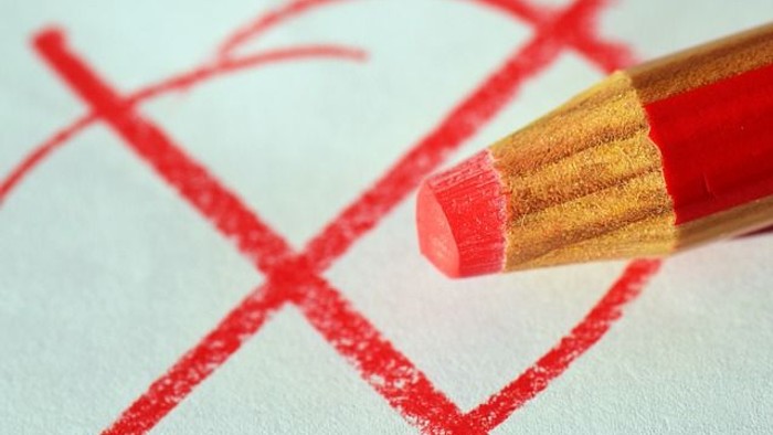 Ein roter Bleistift liegt auf einem Papier mit roten Kreuzen.