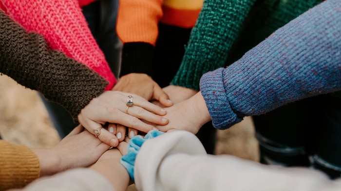 Menschen, die sich im Kreis an den Händen halten und bunte Pullover tragen.