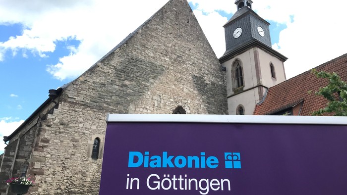 „Schild für die Diakonie in Göttingen mit historischer Kirche und Uhrturm im Hintergrund.“