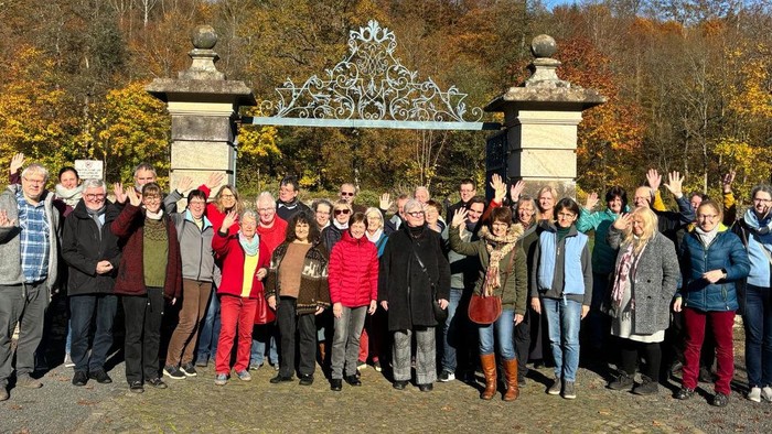 Eine fröhliche Gruppe posiert gemeinsam vor einem verzierten Tor im Herbst und zeigt Friedenszeichen.