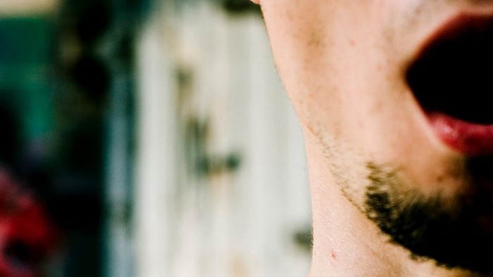 Ein Mann mit Bart und offenem Mund, trägt ein schwarzes Hemd