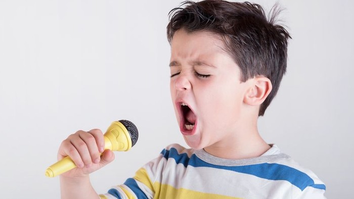 Ein Junge singt laut in ein gelbes Mikrofon.