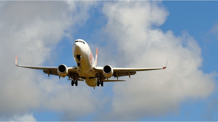 Verkehrsflugzeug im Steigflug mit ausgefahrenem Fahrwerk vor teilweise bewölktem Himmel.