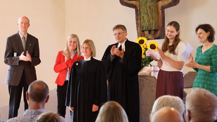 Eine Gruppe von Menschen klatscht während einer formellen Kirchenzeremonie mit einem großen Kruzifix im Hintergrund.
