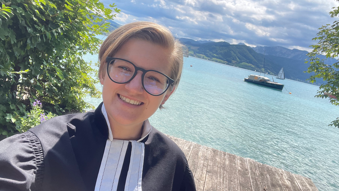 Pfarramtskandidatin Nora Matern im Talar, im Hintergrund der Attersee