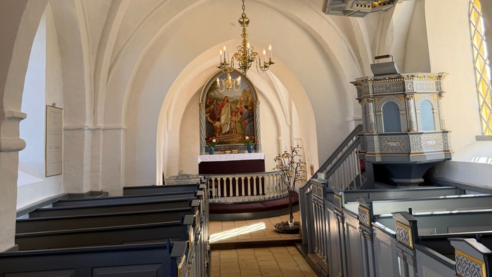 Elegant kirkeinteriør med hvælvede lofter, kirkebænke og prægtige lysekroner, der oplyser alterområdet.