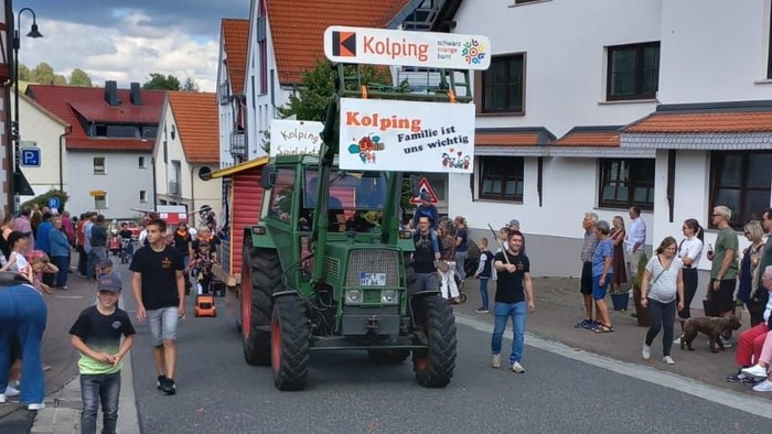 Eine festliche Parade zeigt einen geschmückten Traktor, während Zuschauer eine malerische Dorfstraße säumen.