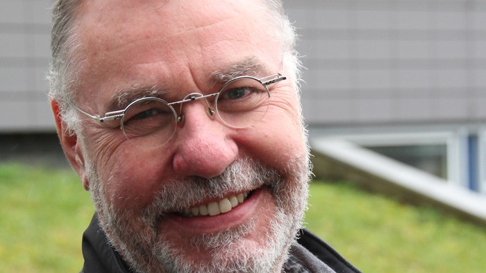Hans-Peter Naumann ist Pfarrer und unterrichtet Religion an einer Schule. Er trägt eine runde Brille und kurzes, graues Haar und einen kurzen Vollbart. Hans-Peter Naumann lächelt auf dem Bild.