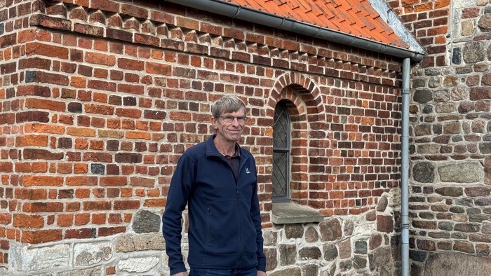 En mand står foran en historisk murstensbygning med et lille buet vindue og en sokkel af sten.