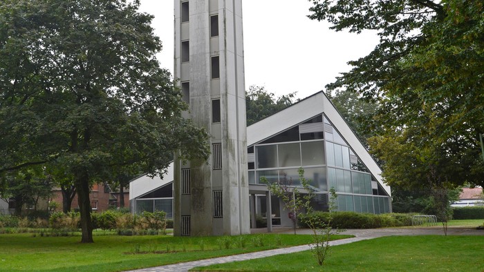 Kreuzkirche Dorsten mit markantem, freistehendem Glockenturm und großer Glasfassade, umgeben von Rasenflächen und alten Bäumen in einer parkähnlichen Anlage.
