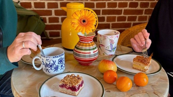 Auf Cafétisch stehen 2 Teller mit Kuchen und Kaffeetassen sowie Obst.