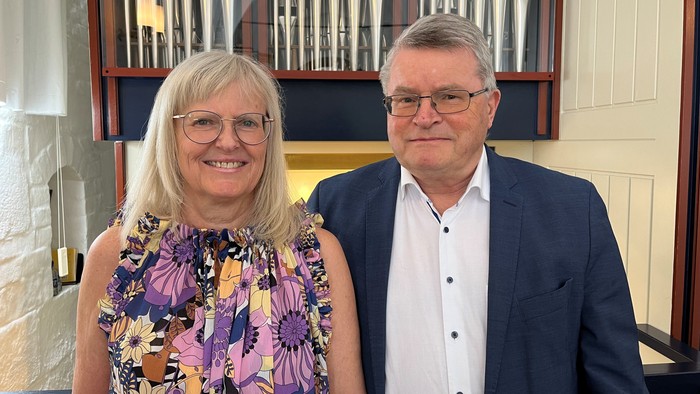 To personer smiler til et foto foran et stort pibeorgel.