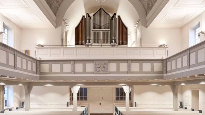 Geräumiges Kircheninneres mit Reihen von Kirchenbänken, erhöhter Orgel und gewölbter Decke.