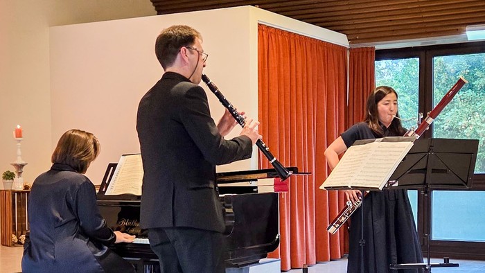 Ein Trio mit Klavier, Klarinette und Fagott spielt in einem großen Saal, gesehen von der Bühnenseite