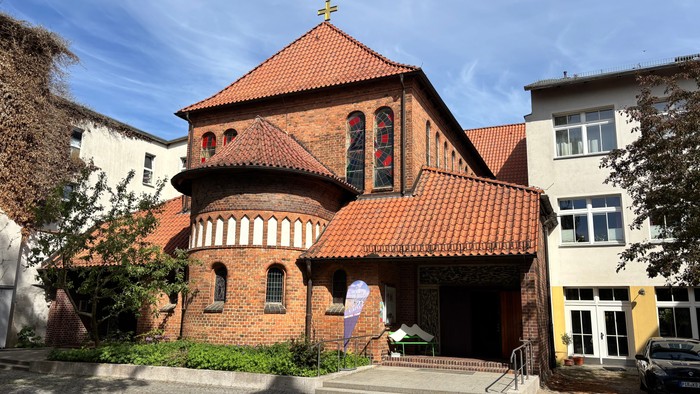 Historische Backsteinkirche mit rotem Ziegeldach und Bogenfenstern in einem malerischen städtischen Umfeld.