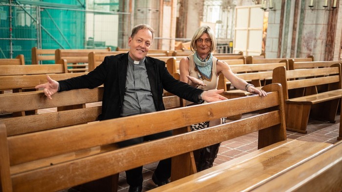 Pastor Robert Pfeifer und Küsterin Paula Claussen sitzen auf den Kirchenbänken in St. Marien, die ab sofort versteigert werden.