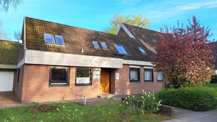 Ein zweistöckiges Haus mit rotem Ziegeldach und einem kleinen Garten.